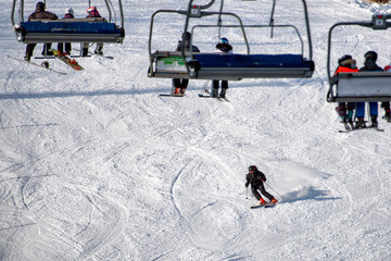 People sitting on chairlift and skiers skiing downhill on slope at mountain resort.