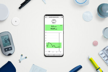 Phone with blood sugar level app surrounded by accessories to keep diabetes under control. Top...