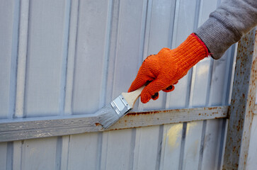 Painting the fence. Woman's hand painting steel fence with a brush