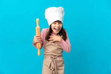 Little girl holding a rolling pin isolated on blue background smiling a lot
