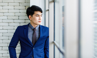 Portrait studio shot Asian handsome professional successful male businessman entrepreneur in formal blue suit necktie standing smiling look at camera on white brick wall background near office window