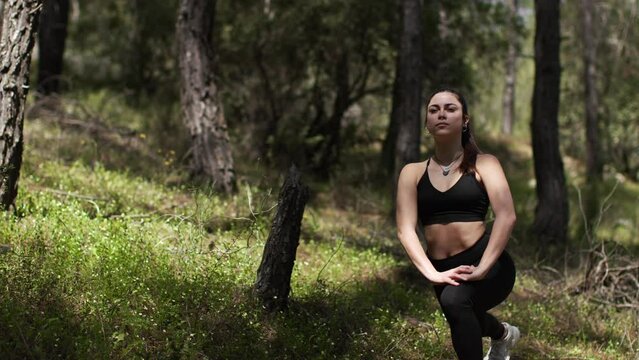 Young brunette woman in black clothes warming up, working out in the forest