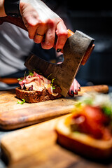 Woman chef hand cutting tasty sandwich with axe on wooden plate