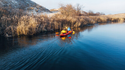 Two man in bright clothes floats on a red kayak on the river. Winter. Ukraine