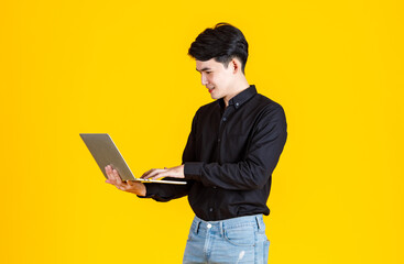 Portrait closeup studio shot of Asian man happy male businessman model in casual outfit standing holding laptop computer for advertising on yellow background