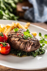 Medium rare sirloin steak on a plate served with spinach, tomatoes and fries