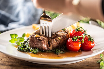 Detail of a fork and knife cut ina juicy perfectly-made steak on a plate.