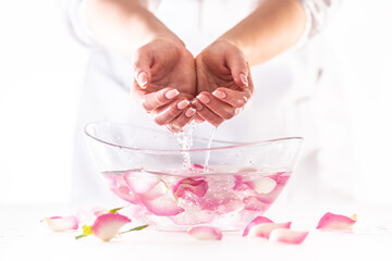 Obraz na płótnie Canvas Female hands lifted from water in a glass bowl full of flower petals in a white environment