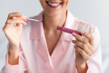 Smiling woman applying lip gloss holding tube, closeup