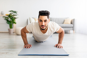 Fototapeta premium Strong young Arab man making strength workout, standing in plank pose at home