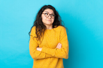Fototapeta premium Teenager Russian girl isolated on blue background making doubts gesture while lifting the shoulders
