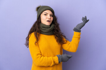 Teenager Russian girl with winter hat isolated on purple background extending hands to the side for inviting to come