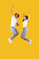 Fototapeta na wymiar Excited millennial couple taking selfie and jumping at studio