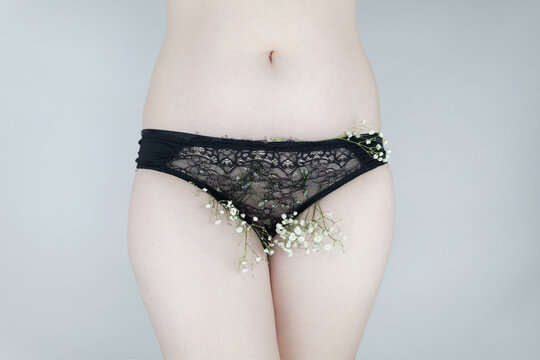 A woman has small flowers sticking out from under her underpants, imitating extra hair. Laser hair removal and shaving with a razor. Conceptual shot about women issues. Proper self care.