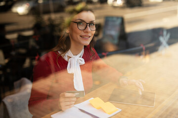 Happy woman using credit card to shopping online with tablet. Beautiful young woman drinking coffee in cafe