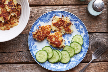 Draniki and cucumbers on a blue plate. Top view, wooden background