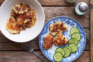 Draniki and cucumbers on a blue plate. Top view, wooden background