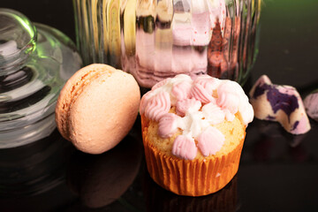 macaroon and cupcake on the table on a dark background near the jars for sweets