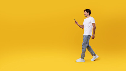 Young man walking with cellphone isolated on yellow wall, panorama