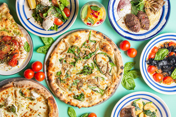 Fototapeta na wymiar Full table of italian meals on plates. Pizza, pasta, ravioli, carpaccio. Over blue background. Top view, flat lay.