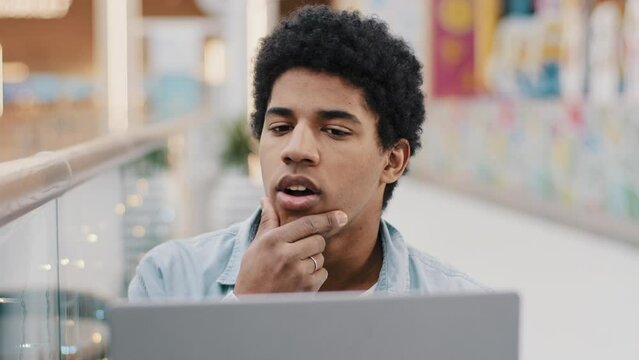 Pensive male african american guy rubbing chin thinking solution problem plan strategy startup idea sitting with laptop indoor male writer composing novel journalist working deep in thought difficulty