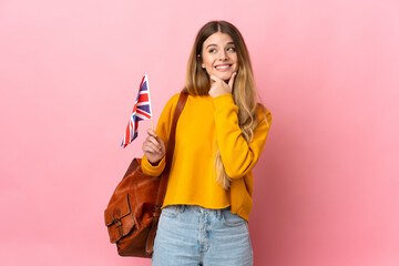 Young blonde woman holding an United Kingdom flag isolated on white background looking to the side...