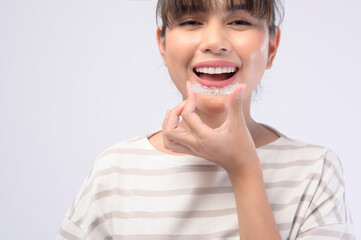 Young smiling woman holding invisalign braces over white background studio, dental healthcare and Orthodontic concept. - obrazy, fototapety, plakaty