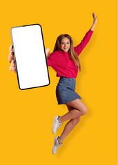 Cheery Caucasian woman jumping in air, showing smartphone with blank white screen over orange...