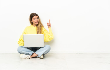 Young woman with a laptop sitting on the floor thinking an idea pointing the finger up