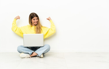 Young woman with a laptop sitting on the floor doing strong gesture