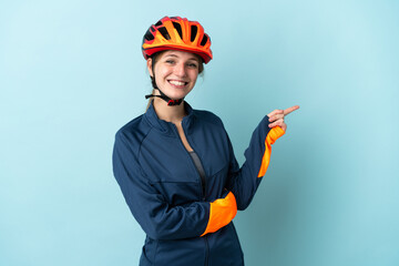 Young cyclist woman isolated on blue background pointing finger to the side - obrazy, fototapety, plakaty