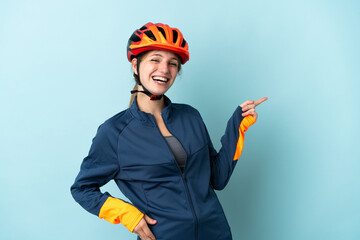 Young cyclist woman isolated on blue background pointing finger to the side and presenting a product - obrazy, fototapety, plakaty