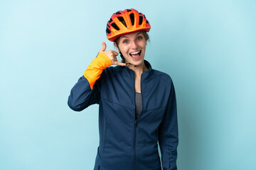 Young cyclist woman isolated on blue background making phone gesture. Call me back sign