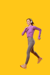 Fototapeta na wymiar Photo of young happy woman running over yellow background and using white wireless headphones.