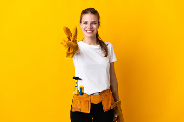 Young electrician woman isolated on yellow background smiling and showing victory sign