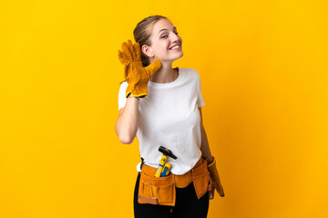 Young electrician woman isolated on yellow background listening to something by putting hand on the ear