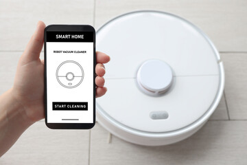 Fototapeta premium Hand control of the robot vacuum cleaner in the app on the mobile phone screen. One-touch home cleaning