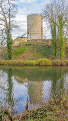 Fototapeta na wymiar Round tower of castle ruins on a hill, bare trees, moat with the tower reflected in the water surface, cloudy day with a hazy blue sky in the background in Stein, South Limburg in the Netherlands