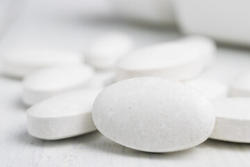 Fototapeta na wymiar White pills at white wooden planks, medication treatment, close-up view