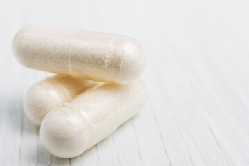 Fototapeta na wymiar White pills or capsules at white wooden planks, medication treatment, alternative medicine, close-up view