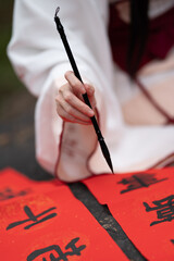 closeup of a hand holding a brush pen and writing Chinese on red paper