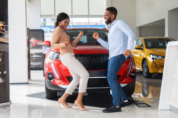 Overjoyed Black Couple Celebrating Buying New Car, Dancing In Dealership Office