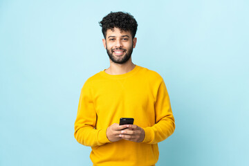 Young Moroccan man isolated on blue background sending a message with the mobile