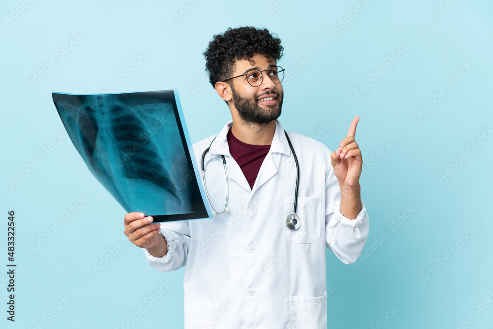 Wall mural young moroccan traumatologist in workplace isolated on blue background pointing up a great idea