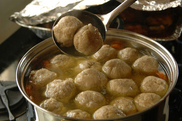 Large pot of chicken soup with plentiful fluffy matzah balls floating on the surface. 