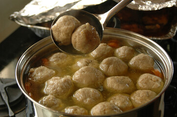 Traditional Jewish holiday meal of chicken soup with plentiful fluffy matzah balls floating on the surface of a large pot. 