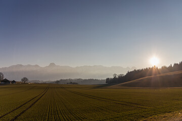 field in front of mountains in sunset with a farm and dust, countryside