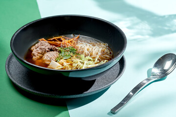 Asian pho bo soup with beef, tofu, noodles and onions in a plate of bright backgrounds. Selective focus, hard light