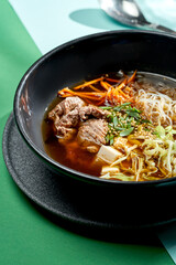 Asian pho bo soup with beef, tofu, noodles and onions in a plate of bright backgrounds. Selective focus, hard light
