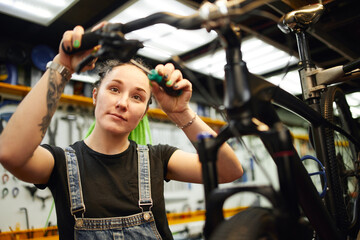 Fototapeta na wymiar Smiling woman repairing bike in workshop